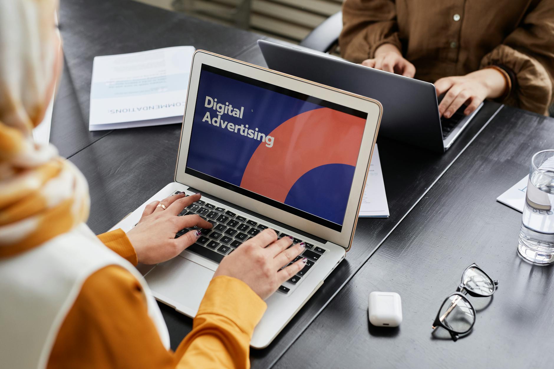 Two professionals reviewing paid ads campaign data on laptops in an office.