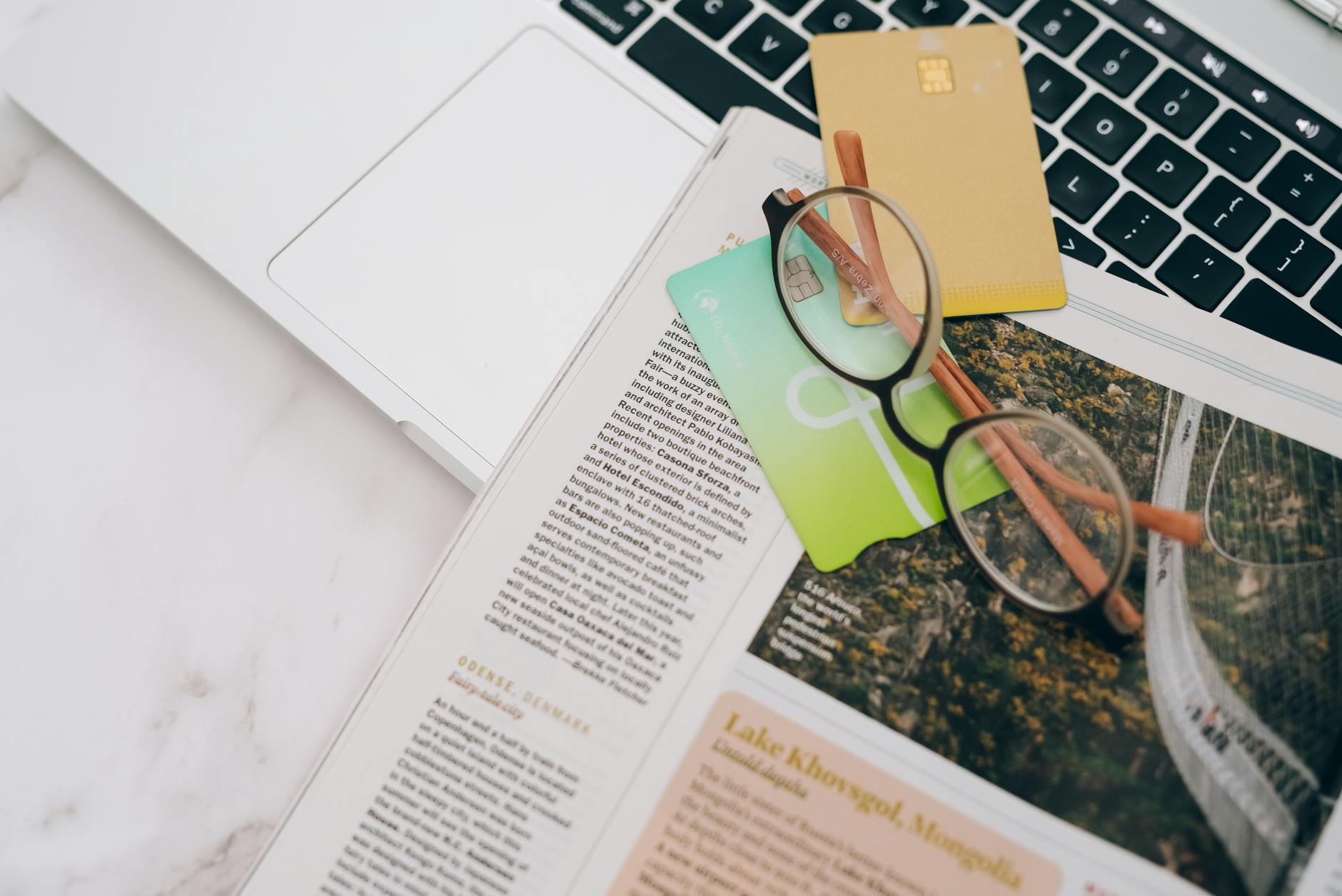 Eyeglasses and credit cards on a magazine beside a laptop